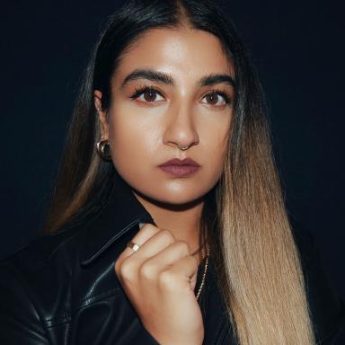 Woman with long straight ombré coloured hair faces camera with right hand clasped onto her black jacket's collar